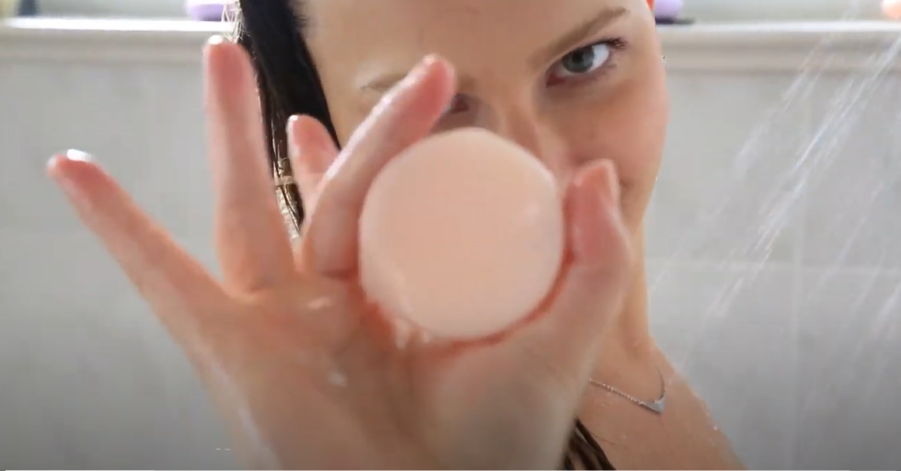 Tangie conditioner bar held in hand – pink unscented bar Woman holding a round pink Tangie conditioner bar in front of her face