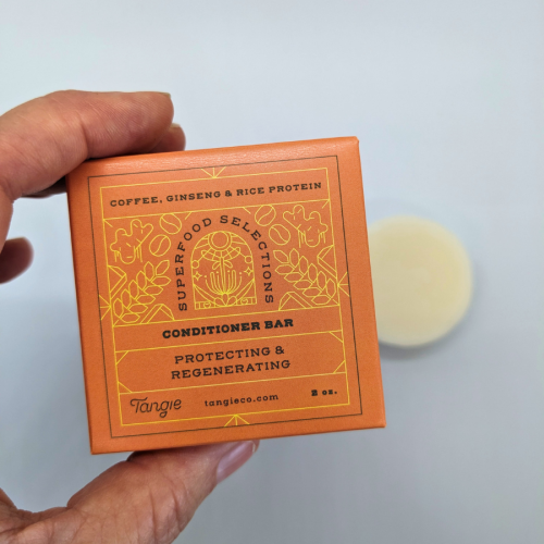 Hand holding Tangie Superfoods Conditioner Bar box with solid conditioner bar in background, showcasing plastic-free haircare packaging.