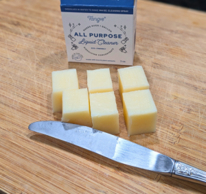 Tangie all-purpose cleaner concentrate bar cut into six pieces on a wooden cutting board with a knife.