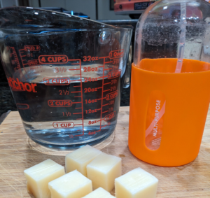 Tangie all-purpose cleaner concentrate pieces with a measuring cup of water and a reusable orange spray bottle.