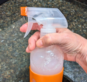 Hand holding a reusable spray bottle filled with Tangie’s all-purpose cleaner on a black countertop.